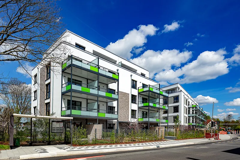 Modernes Mehrfamilienhaus mit Balkonen und leuchtend grünen Fassadenelementen